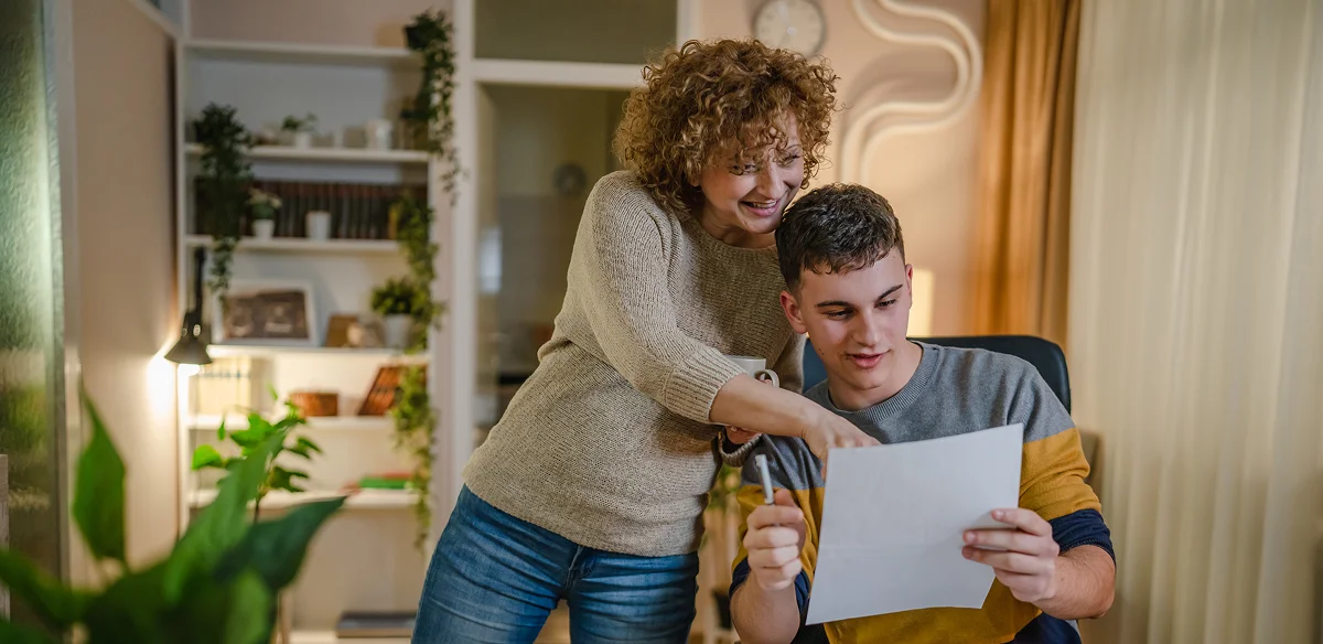 A woman with curly hair and a young man in a casual sweater smile